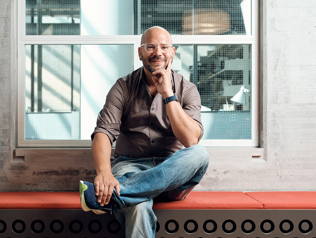 Ein Mann mit Brille sitzt lächelnd auf einer Bank