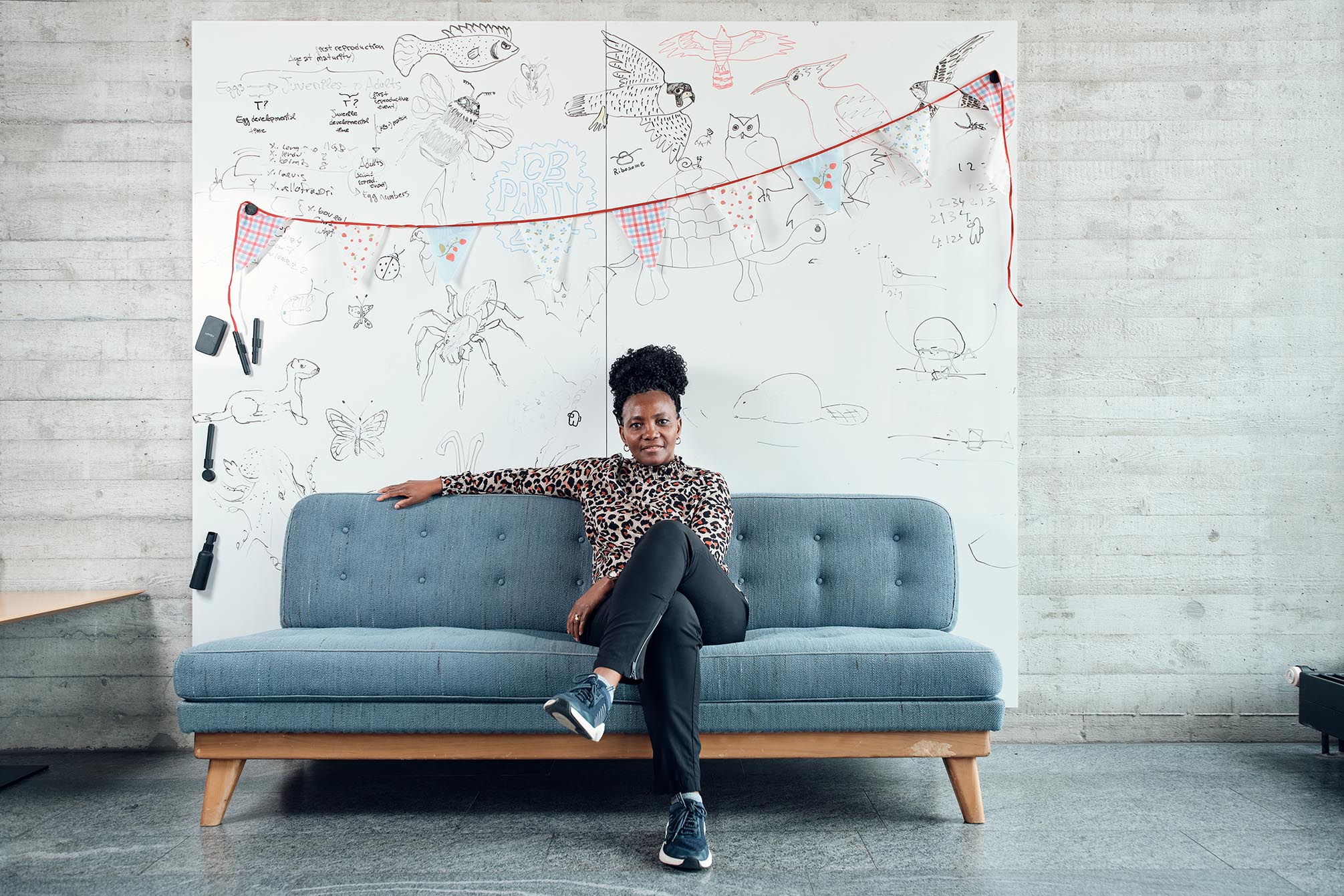 Eine Frau sitzend auf einem Sofa, hinter ihr eine Wand mit Kinderzeichnungen.