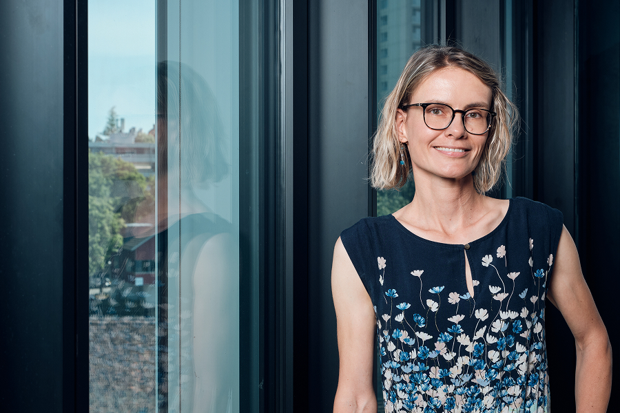 Frau mit Brille steht am Fenster und lächelt.