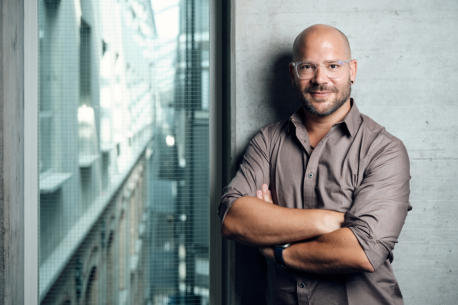 Ein Mann mit verschränkten Armen steht vor einer Wand.