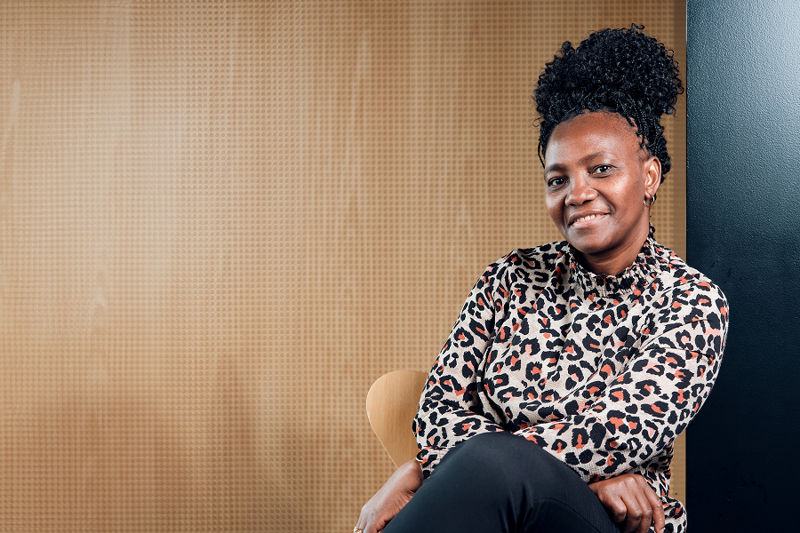 Eine Frau sitzt vor einer Wand aus Holz und lächelt.