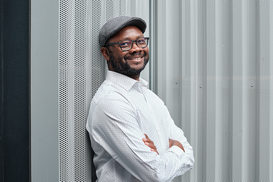 Eine Aussenaufnahme von einem Mann mit Hut und Brille, der lächelt.