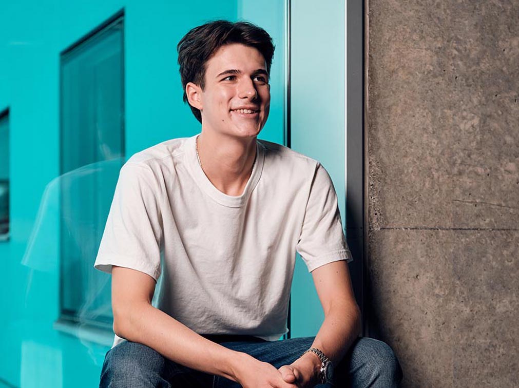 Ein junger Mann sitzt vor einem grossen Glaswand.