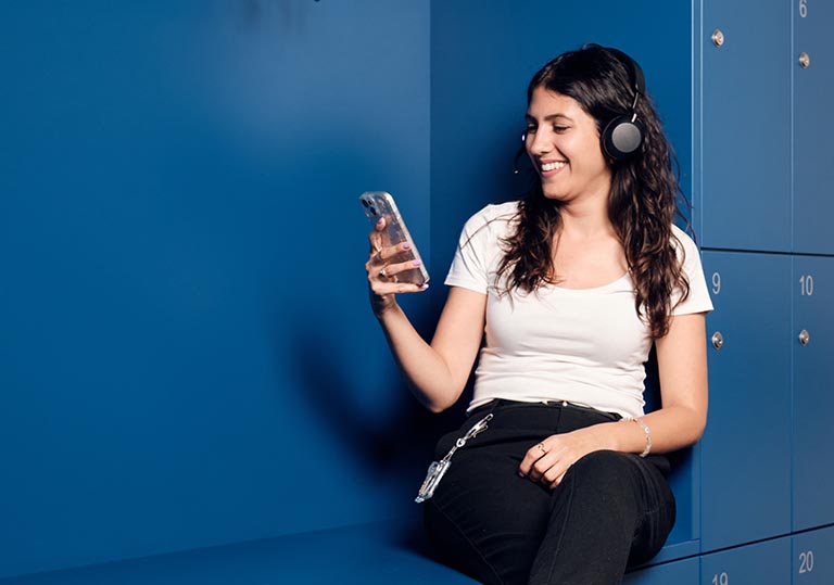 Eine junge Frau mit Kopfhörern schaut in ihr Phone und lächelt.