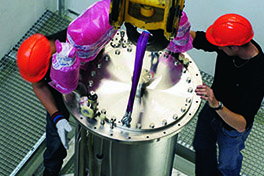 Drei Personen mit Schutzhelmen montieren einen grossen Stahlzylinder