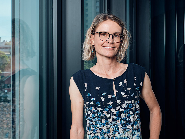 Eine lächelnde Frau steht am Fenster.