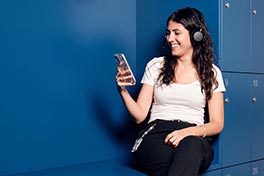 Junge Frau sitzt, hat Köpfhörer und schaut in das Handy.